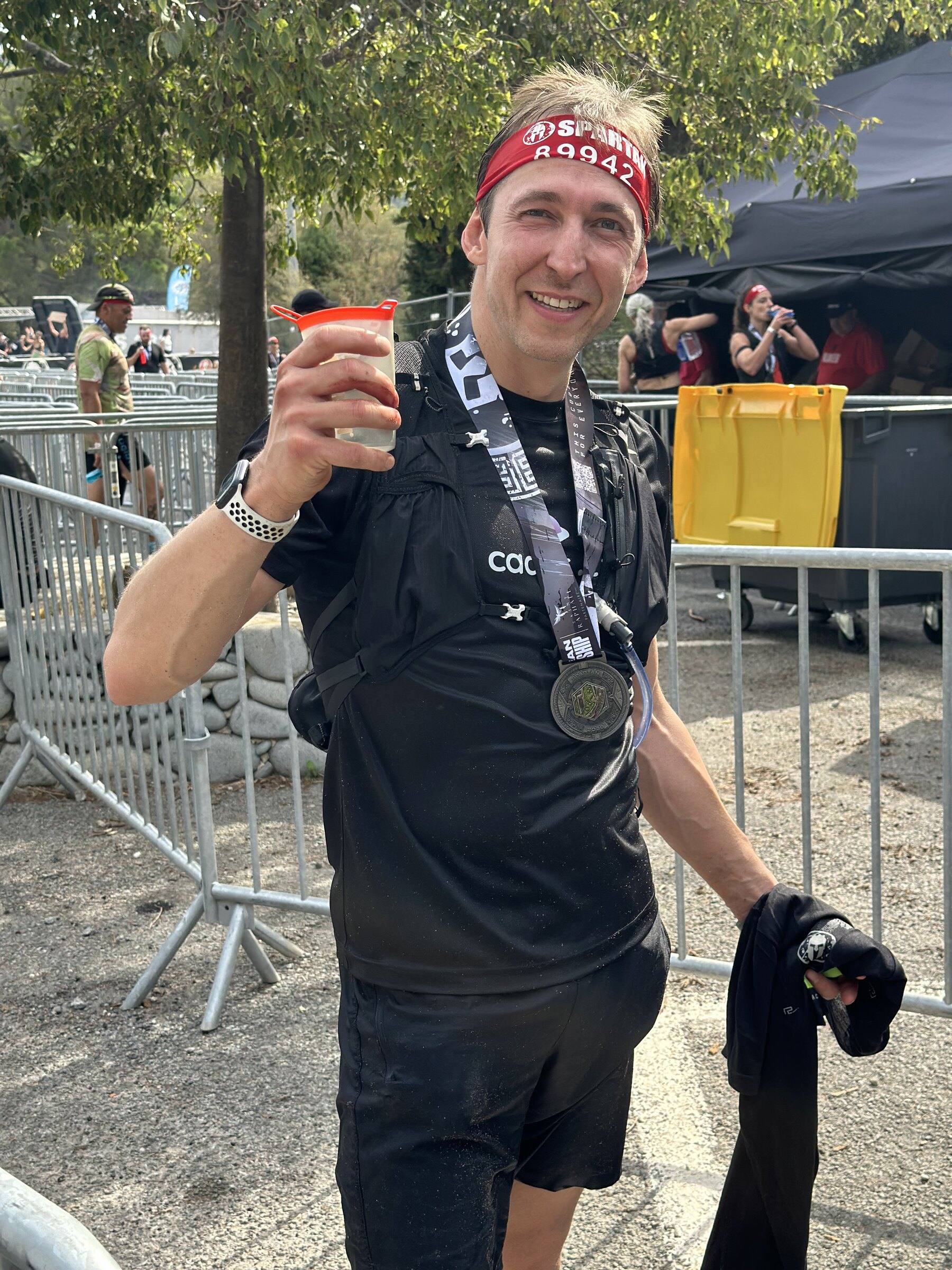 Antoine, médaille autour du cou, un verre à la main, pieds nus après l’arrivée