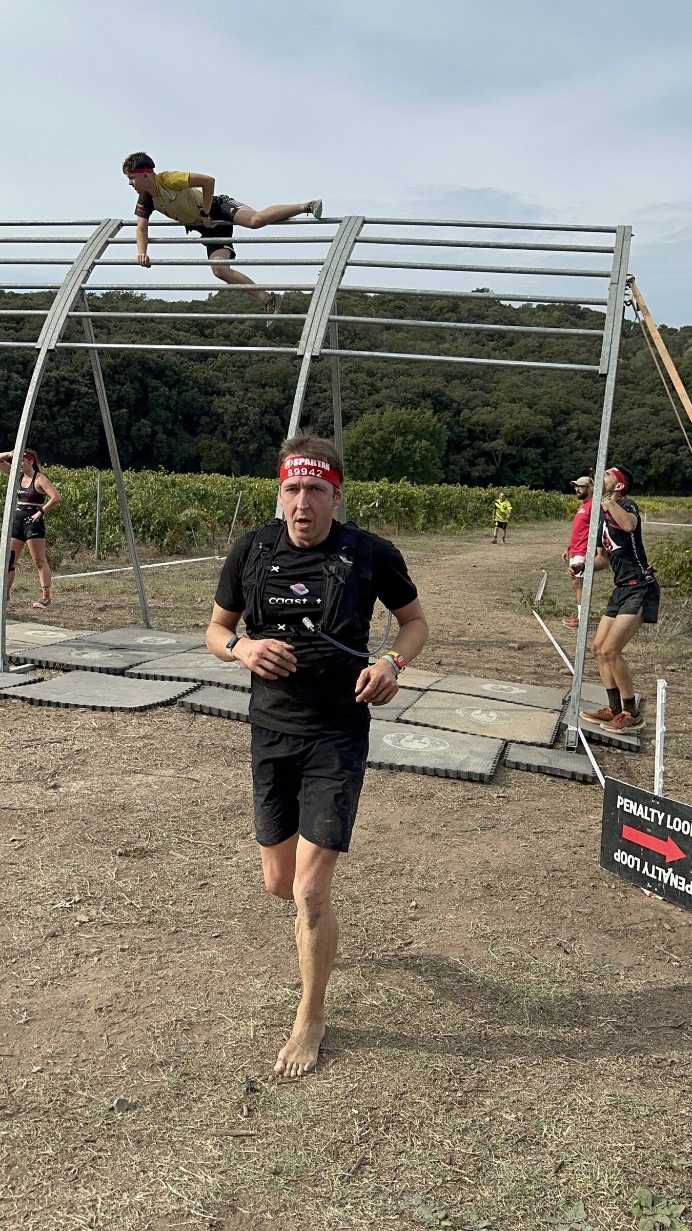 Antoine court pieds nus sous une structure d’obstacle en tubes métalliques