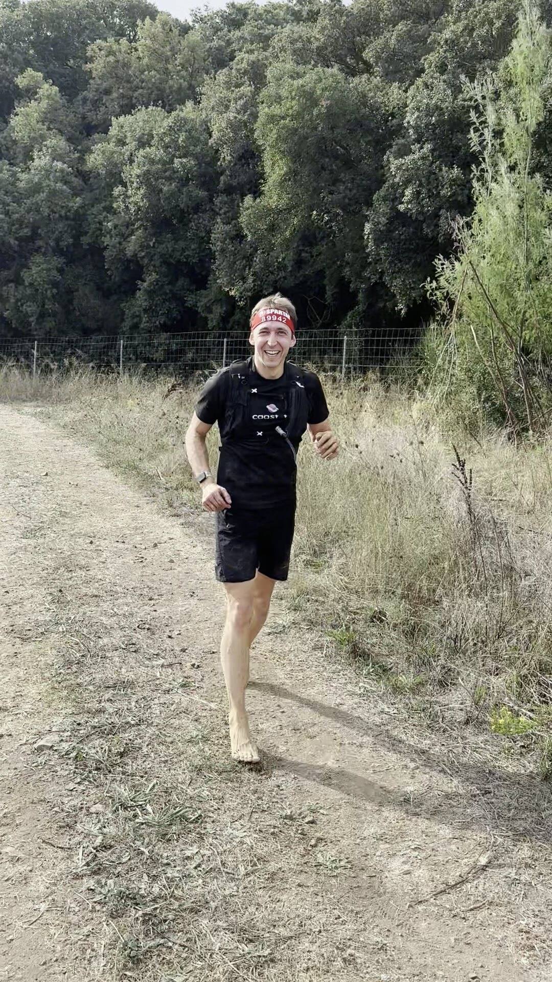 Antoine court pieds nus vers la caméra sur un chemin de terre bordé d’herbes sèches
