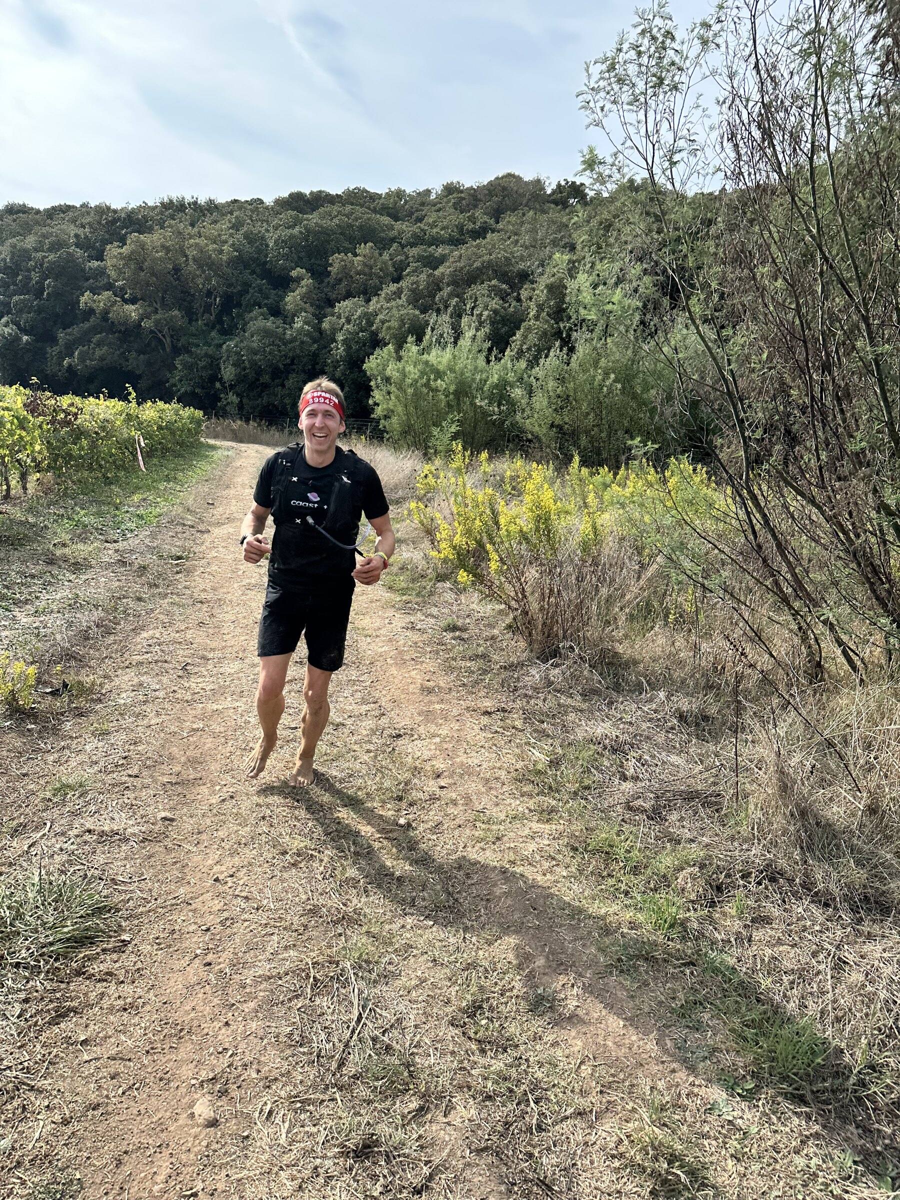 Antoine court pieds nus vers l’objectif sur un large chemin de terre bordé de vignes et de maquis