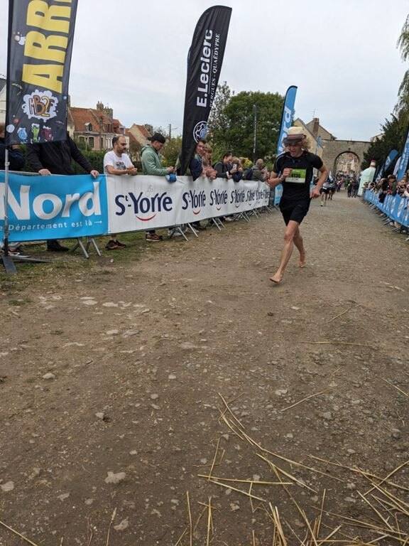 Antoine arrive pieds nus sur un chemin de terre devant les banderoles du semi-marathon de Bergues